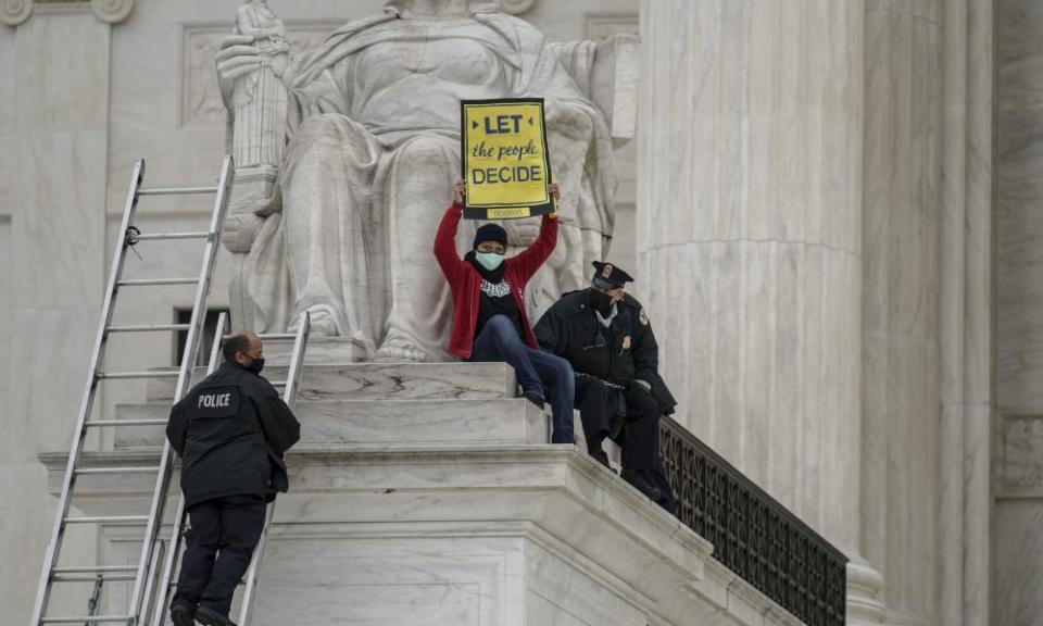 A protester opposed to the Senate’s race to confirm Amy Coney Barrett is removed by police after chaining themselves to a railing and holding a sign while sitting atop the statue Contemplation of Justice, at the Supreme Court on Sunday.