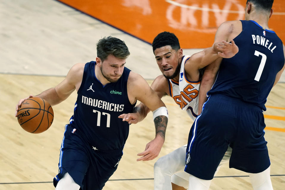 Dallas Mavericks guard Luka Doncic (77) uses the pick by Dwight Powell (7) to drive past Phoenix Suns guard Devin Booker during the first half of an NBA basketball game Wednesday, Dec. 23, 2020, in Phoenix. (AP Photo/Rick Scuteri)