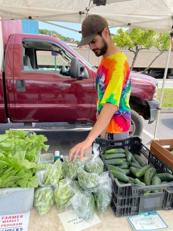 Brian Pacheco, a market worker for the Killam & Bassette Farmstand of Glastonbury, shows some of the produce at the Downtown Norwich Farmer's Market in this file photo