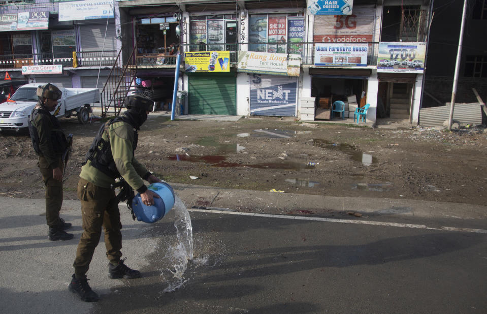 An Indian soldier washes blood stains on a road at the site of an attack on the outskirts of Srinagar, Indian controlled Kashmir, Thursday, March 25, 2021. Rebels fighting against Indian rule in disputed Kashmir Thursday attacked a paramilitary patrol, killing two soldiers and injuring two others, an official said. (AP Photo/Mukhtar Khan)