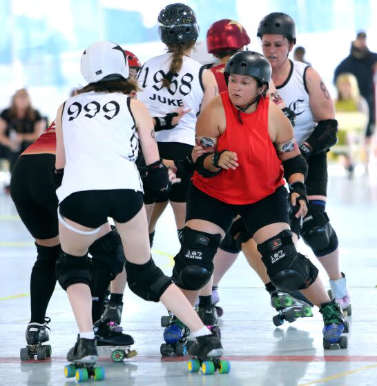 Roller derby El bloqueador del equipo Rocket Queens #185 Bash-n-Smash (Janeet (cq) Juarez), a la derecha, bloquea al bloqueador del equipo Misery Loves Company durante el Fuego Latino Roller Derby el 20 de julio de 2013 en la pista de hockey del parque Charles H. Wilson en Torrance.