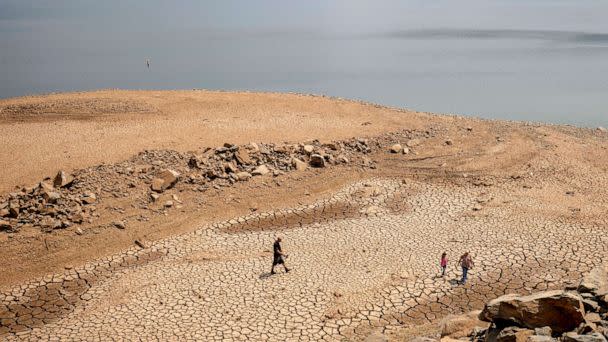 PHOTO: A family walks over cracked mud near Lake Oroville's shore as water levels remain low due to continuing drought conditions, Aug. 22, 2021, in Oroville, Calif. (Ethan Swope/AP, FILE)