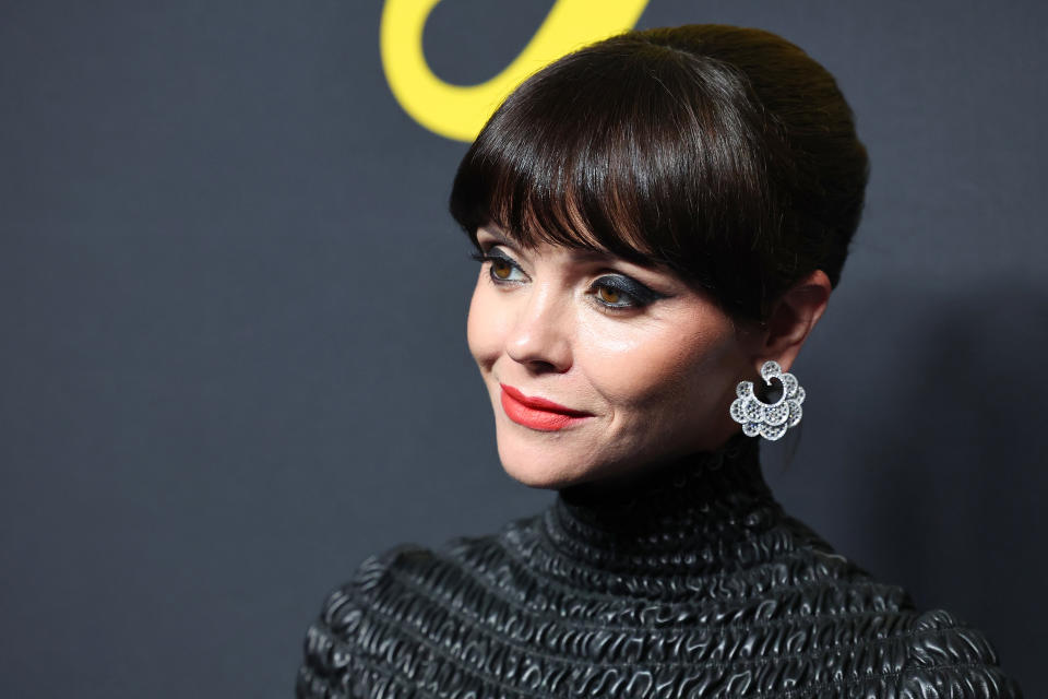 Close-up of Christina with a bob haircut and large earrings, wearing a high-neck textured outfit