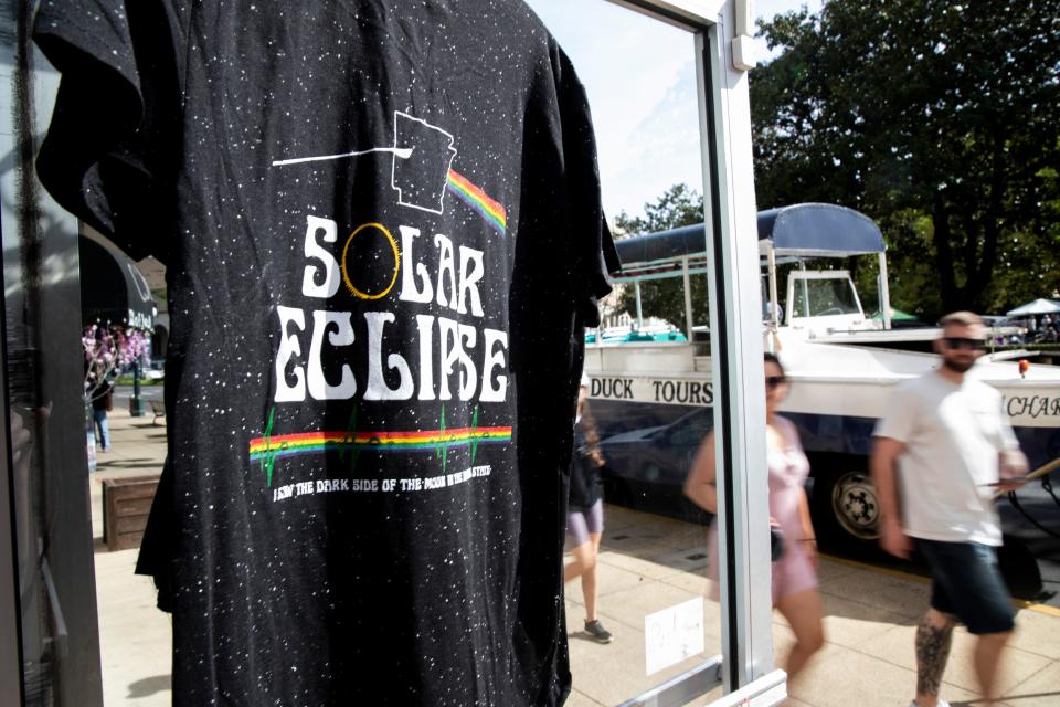 A solar eclipse-themed shirt hangs in the doorway of Snazzies Inc. as people walk by before the total solar eclipse in Hot Springs, Arkansas on Monday, April 8, 2024.