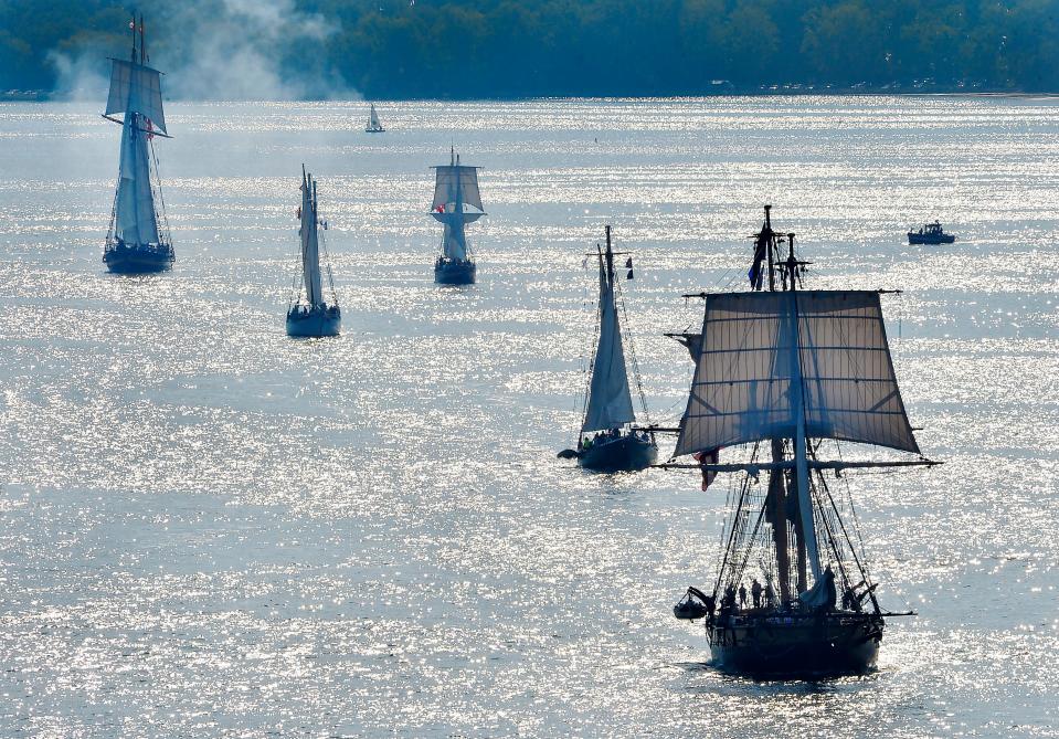 The U.S. Brig Niagara, lower right, leads the Parade of Sail, kicking off Tall Ships Erie 2022, in Erie on Aug. 25, 2022. Four ships following the Niagara were also heading east after making a turn in Presque Isle Bay. Smoke rises after a cannon was fired from the Pride of Baltimore II, top left.