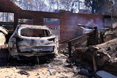 Smoke rises near a destroyed car and home after a bushfire swept through the town of Tathra, located on the south-east coast of New South Wales in Australia, March 19, 2018. AAP/Dean Lewins/via REUTERS