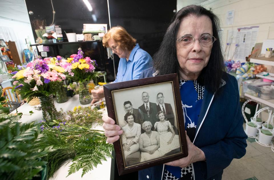 Grandview Florist owner Carolyn Brewton shows a photo of her family as longtime employee Jean Huff works on a flower arraignment at the shop, which celebrated its 100th anniversary this month.
