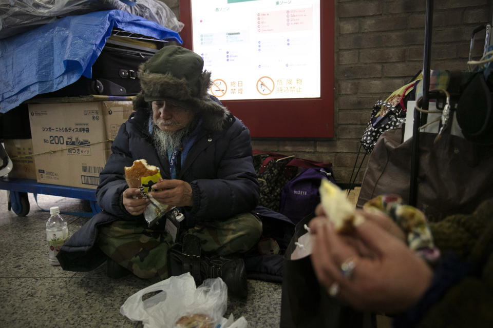In this Wednesday, Jan. 15, 2020, photo, Masanori Ito, a 76-year-old homeless man, eats his late dinner with his friend before bedding down for the night at Shinjuku Station in Tokyo. The dozens of homeless people sleeping rough in shuttered Tokyo subway stations worry that with Japan's image at stake authorities will force them to move ahead of the Olympics. (AP Photo/Jae C. Hong)
