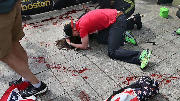 A man comforts a victim on the sidewalk at the scene of the first explosion.