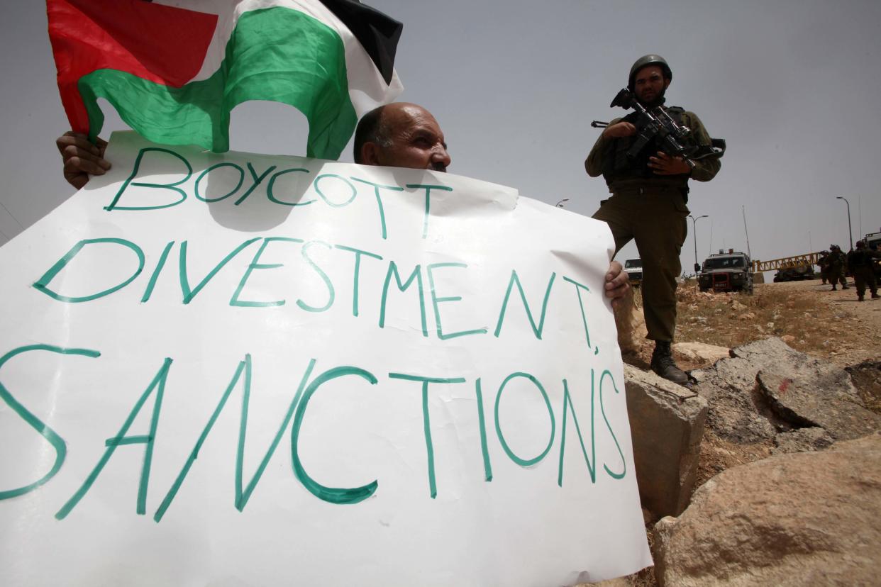 <p>A Palestinian holds a placard that reads ‘Boycott, divestment, sanctions’</p> (AFP via Getty Images)