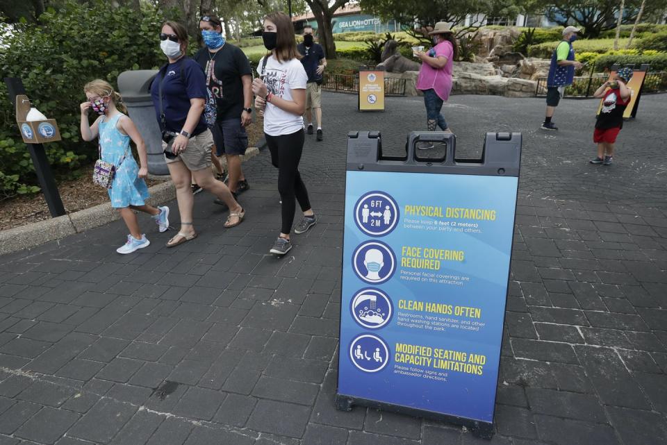 A family wearing masks walking past a sign about social distancing, mask-wearing and hand-washing.