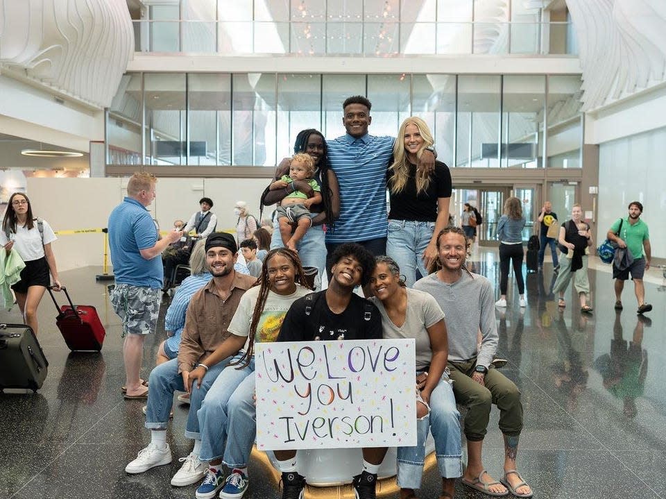 a group of people at an airport holding a sign that says "we love you, iverson!"