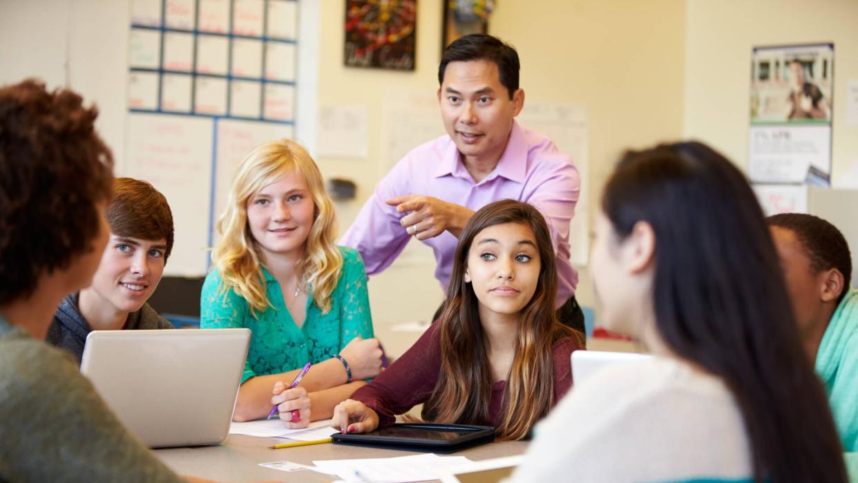 High School Students With Teacher In Class Using Laptops Smiling.