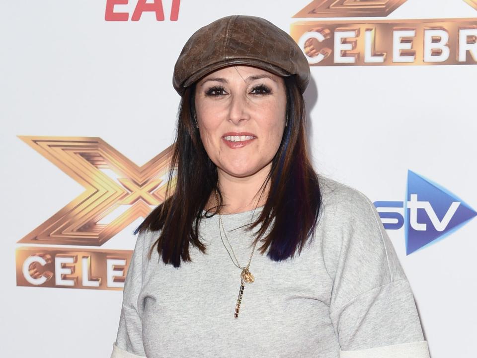 Ricki smiling with a hat on and t-shirt in front of a backdrop.