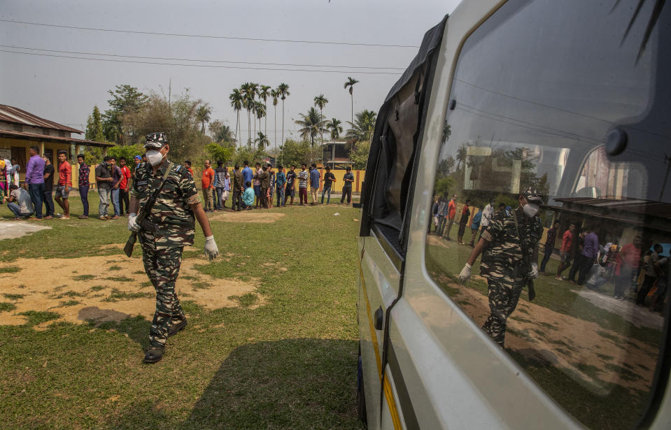 An Indian paramilitary person walks past people standing in queue to cast their votes in a polling station during the third phase of assembly election in Gauhati, India, Tuesday, April 6, 2021. Voters in four Indian states and a union territory are casting their ballots, in elections seen as a test for Prime Minister Narendra Modi’s government which is battling the latest surge in coronavirus cases. (AP Photo/Anupam Nath)