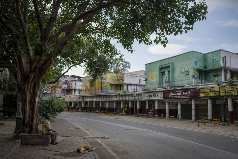A dog lies by a man resting under a tree at a deserted market area as traffic restrictions and diversions are placed ahead of the weekend's G20 Summit, in New Delhi, India, Friday, Sept. 8, 2023. (AP Photo/Altaf Qadri)