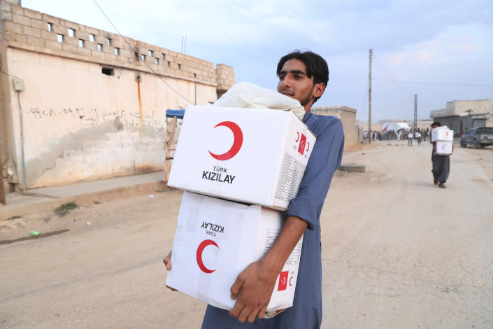 In this image provided by Turkish Red Crescent, a youth carries aid being distributed by Turkish Red Crescent in Ras Al-Ayn, Syria, Saturday, Oct. 19, 2019. Turkish Red Crescent says it has delivered humanitarian aid for 2000 people in Ras Al-Ayn, including flour with other food and hygiene materials to follow. The organisation said it also provided aid to Tal Abyad and will continue to do so in areas cleared by the Turkish and the Turkish-backed forces, from fighters from Kurdish People's Protection Units, or YPG. (Fatih Isci/Turkish Red Crescent via AP)