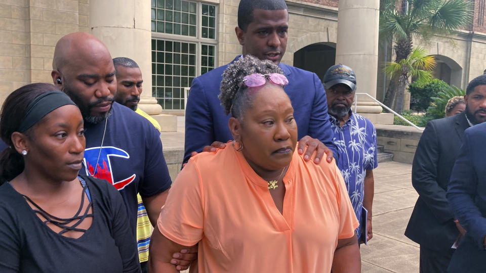 Betty James, center, is comforted by one of her attorneys, Bakari Sellers (standing behind her with hands on her shoulders) and family members during a news conference in Woodbine, Ga., on Monday, Aug. 22, 2022, to announce a federal lawsuit against the Camden County sheriff and others. James' daughter, Latoya James, was killed by gunfire after Camden County deputies executed a drug warrant at her cousin's home on May 4, 2021. The lawsuit says deputies violated the slain woman's civil rights by failing to give the home's occupants time to answer the door. (AP Photo/Russ Bynum)