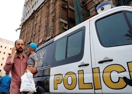 An Egyptian man carries his son with cancer as he walks past a police car in front of the damaged facade of the National Cancer Institute, after an overnight fire from a blast, in Cairo