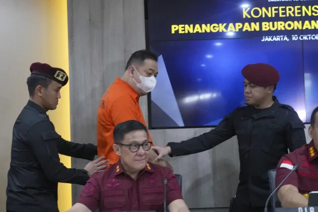 Chinese fugitive identified only by his initial LQ wears a mask escorted by Immigration officers during a news conference in Jakarta, Indonesia, Thursday, Oct. 10, 2024. (AP Photo/Tatan Syuflana)