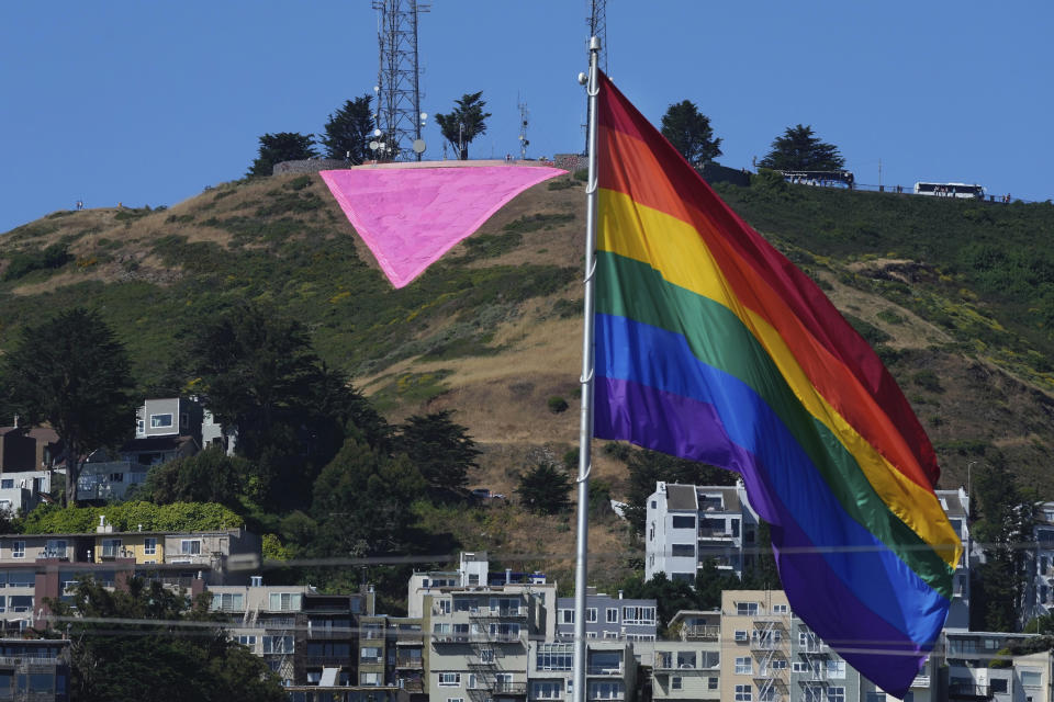 A pink triangle is seen on top of Twin Peaks behind the Castro district rainbow flag in San Francisco, Tuesday, June 20, 2023. Hundreds of volunteers installed the giant pink triangle made out of cloth and canvas and with pink lights around its edges last week as part of the city's Pride celebrations. It's an annual tradition that started in 1995 but this year's triangle is nearly an acre in size and can be seen up to 20 miles (32 kms.) away. (AP Photo/Jeff Chiu)