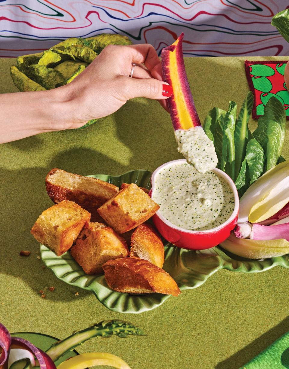 Two hands dipping vegetables into a bowl of sauce with two martinis and background patterns