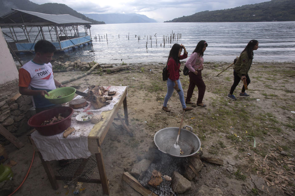 In this Saturday, Oct 26, 2019, photo, visitors walk past a man cooking pork by Lake Toba during Toba Pig and Pork Festival in Muara, North Sumatra, Indonesia. Christian residents in Muslim-majority Indonesia's remote Lake Toba region have launched a new festival celebrating pigs that they say is a response to efforts to promote halal tourism in the area. The festival features competitions in barbecuing, pig calling and pig catching as well as live music and other entertainment that organizers say are parts of the culture of the community that lives in the area. (AP Photo/Binsar Bakkara)