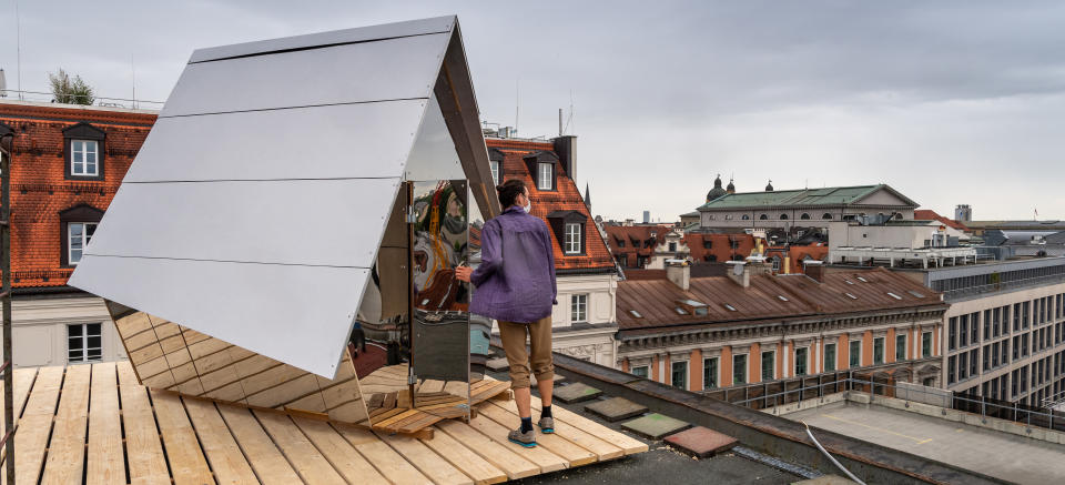 Jakob Wirth steht vor seiner Holzhütte, die auf dem Dach eines Parkhauses in der Innenstadt Münchens steht und mit dem der Künstler auf die hohen Mieten in der Landeshauptstadt aufmerksam machen will. Foto: Peter Kneffel / dpa