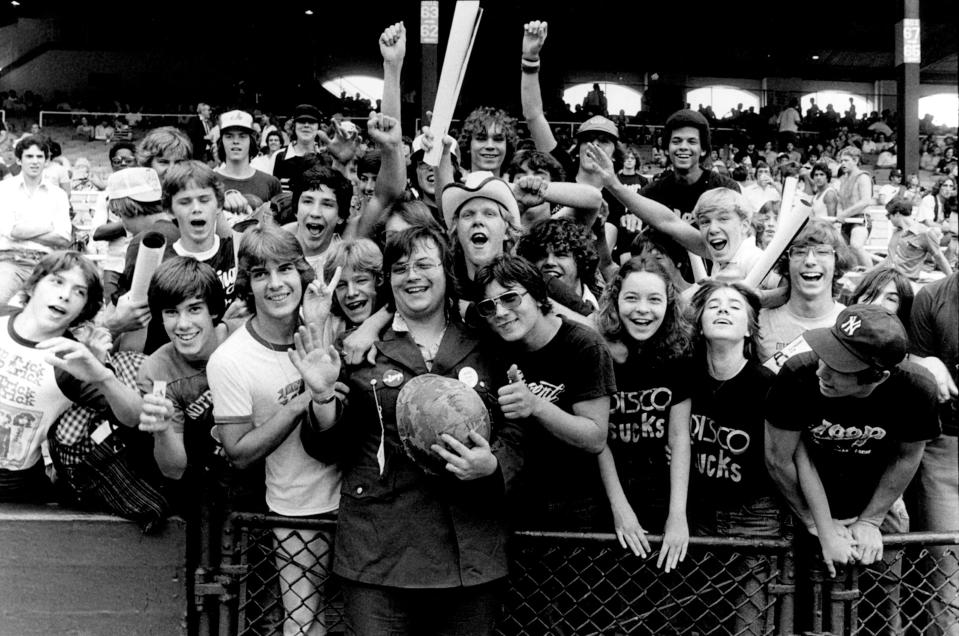 View of the crowd, some wearing 'Disco Sucks' and WLUP 'The Loop' t-shirts, surrounding Chicago DJ Steve Dahl, wearing military clothing and holding a helmet, during the anti-disco promotional event Disco Demolition Night, held in between games of a nighttime doubleheader between the Chicago White Sox and the Detroit Tigers, Chicago, Illinois, July 12, 1979. (Photo: Paul Natkin/Getty Images)