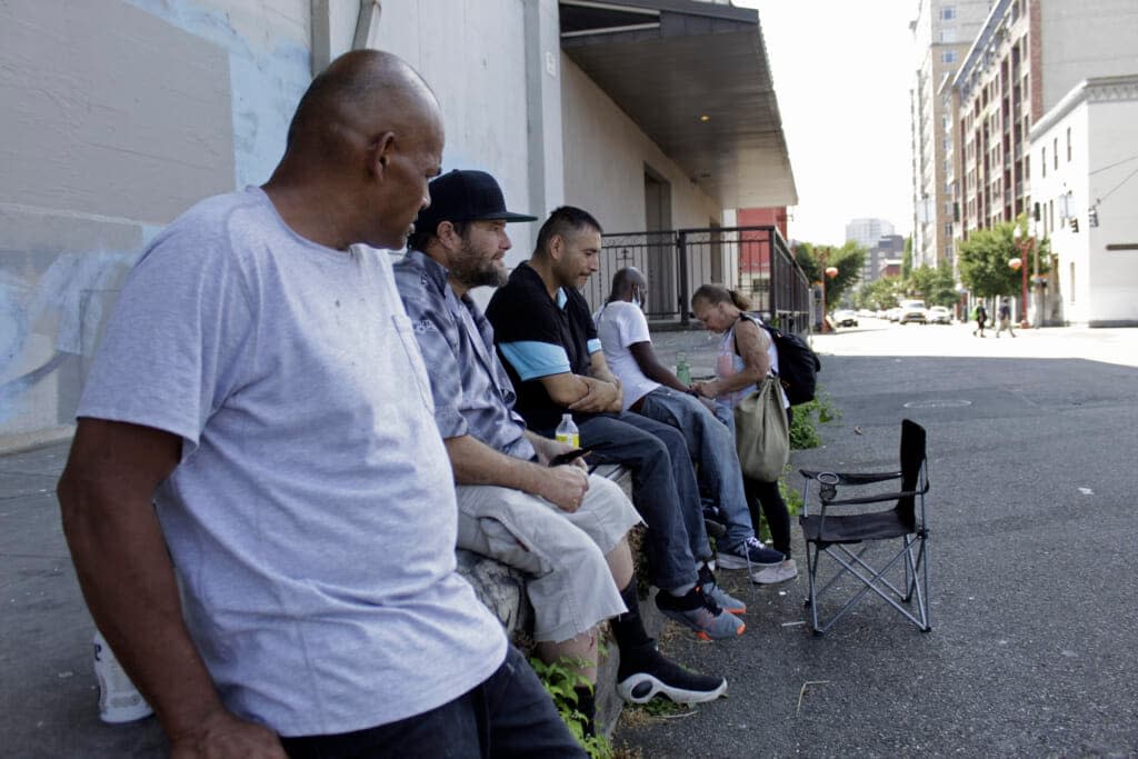 William Nonluecha, foreground, and his friends sit in the shade, Wednesday, July 27, 2022, in Portland, Ore., as a heat wave envelopes the Pacific Northwest. (AP Photo/Gillian Flaccus)