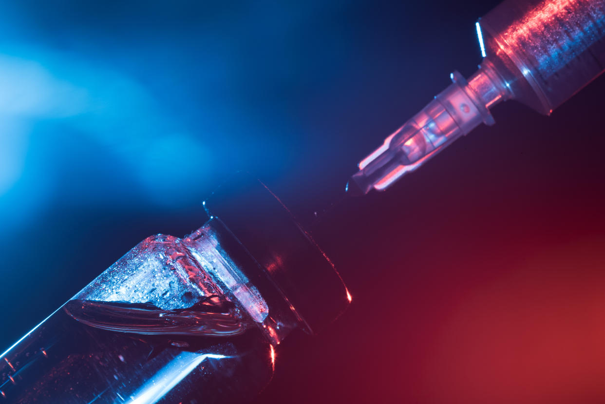 A glass medical bottle with a vaccine and a disposable syringe in color light. A conceptual photo about the danger of viral diseases