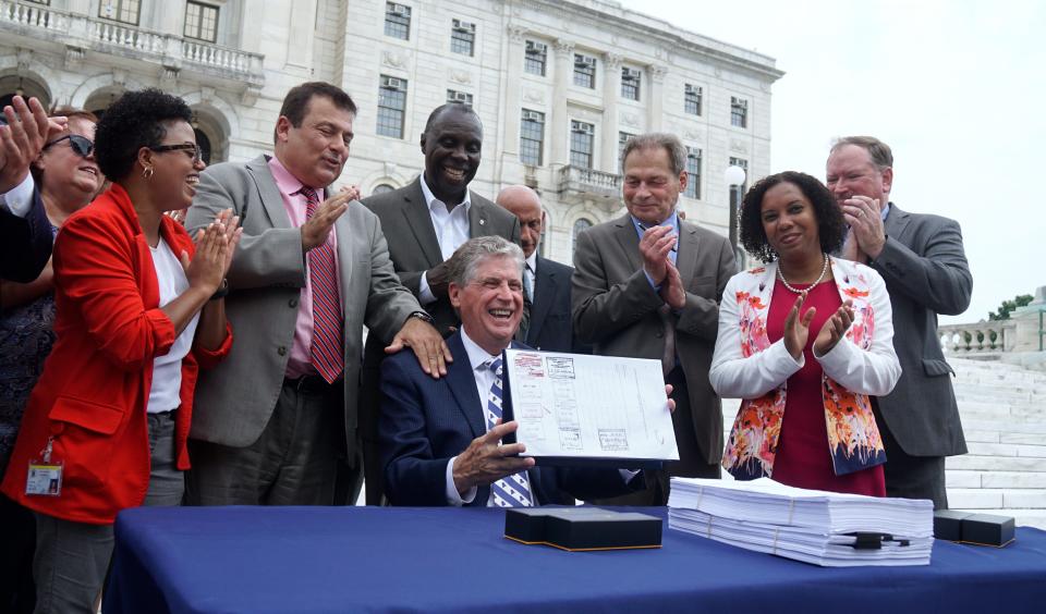 Surrounded by lawmakers who helped craft it, Gov. Dan McKee holds up the freshly signed budget at the State House on Tuesday for the year that began July 1.