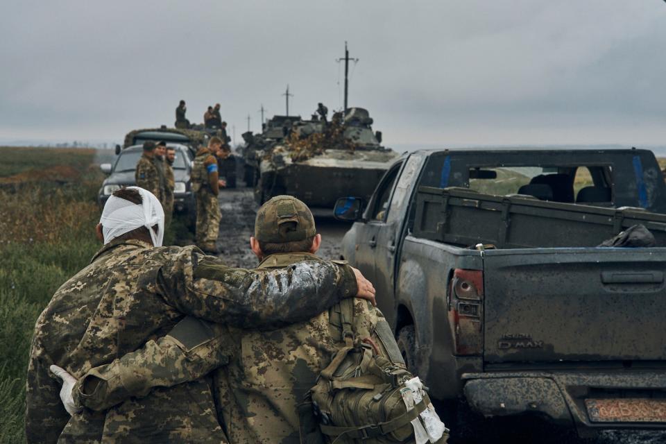 A Ukrainian soldier helps his wounded fellow soldier while military vehicles move on the road in the freed territory in the Kharkiv region, Ukraine, Monday, Sept. 12, 2022.