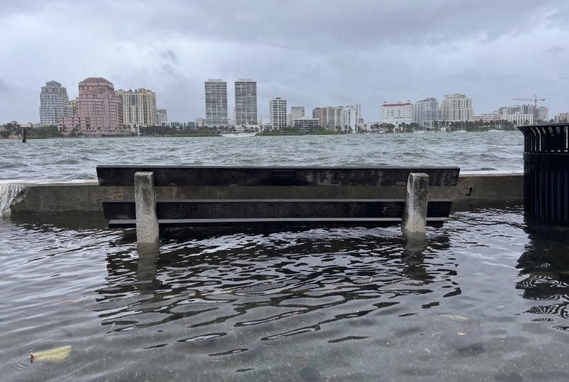 Water from the Intracoastal Waterway tops the seawall and surrounds a bench on the Lake Trail in Palm Beach Wednesday before Hurricane Nicole struck near Vero Beach.