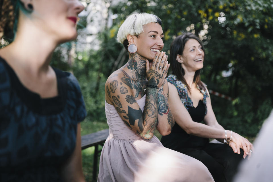 Tattooed wedding guest clasping her hands together as lesbian couple gets married.