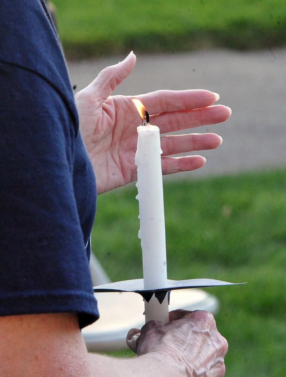 An attendee tries to block the breeze so the candle continues to burn during a vigil Tuesday evening.