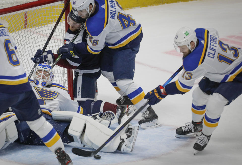 St. Louis Blues left wing Kyle Clifford (13) gathers the puck as Blues goaltender Ville Husso (35) sprawls in the crease and defenseman Jake Walman (46) pins Colorado Avalanche left wing Gabriel Landeskog (92) during the first period of an NHL hockey game in Denver, Saturday, April 3, 2021. (AP Photo/Joe Mahoney)