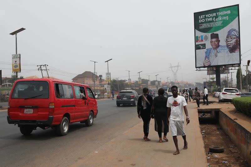 People walk past a campaign billboard of All Progressives Congress (APC) Presidential candidate, Bola Tinubu, ahead of Nigeria's Presidential election in Awka