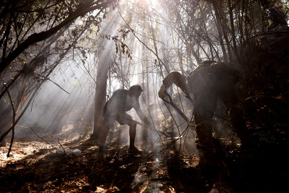 two people put out a fire in a shadowy forest as light streams in from above