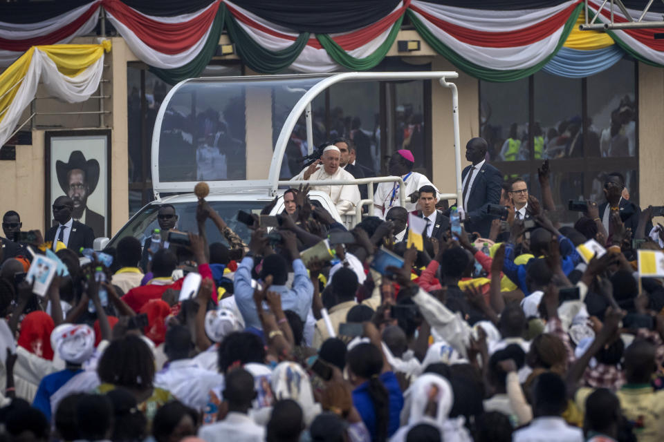 Pope Francis waves next to a photograph of South Sudan's President Salva Kiir, left, as he tours the audience in his vehicle after arriving for a Holy Mass at the John Garang Mausoleum in Juba, South Sudan Sunday, Feb. 5, 2023. Pope Francis is in South Sudan on the final day of a six-day trip that started in Congo, hoping to bring comfort and encouragement to two countries that have been riven by poverty, conflicts and what he calls a "colonialist mentality" that has exploited Africa for centuries. (AP Photo/Ben Curtis)