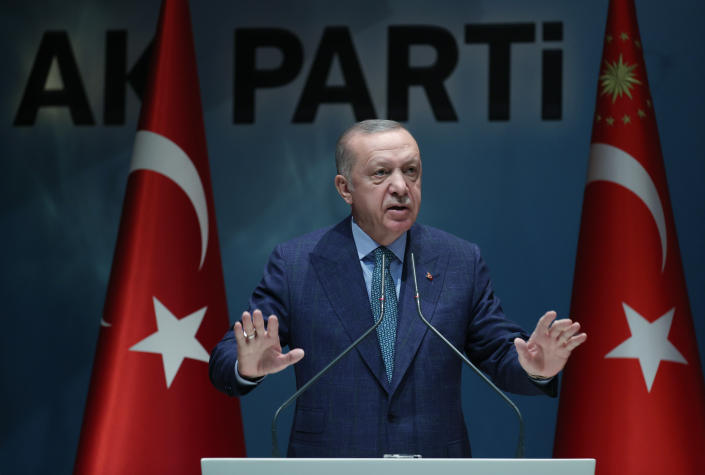Recep Tayyip Erdogan speaks into microphones at a podium in front of flags.