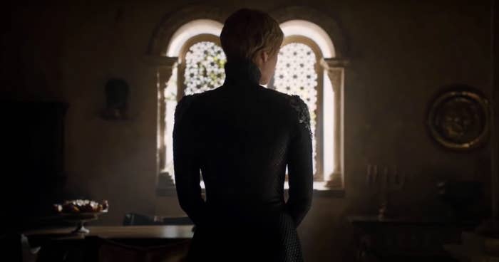 Cersei Lannister stands with her back to the camera in front of two arched windows