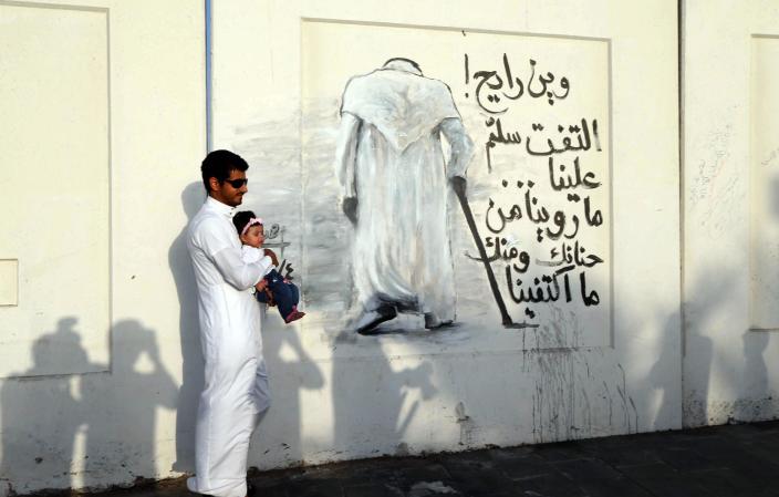 A Saudi carrying his baby poses at a mural dedicated to late King Abdullah with a slogan reading "Where are you going? Look back and say hello. We didn't get enough of you," on January 26, 2015 in the coastal city of Jeddah (AFP Photo/)