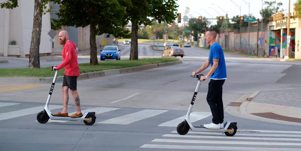 Two men cross E.K. Gaylord Boulevard on Sheridan Avenue on E-scooters in downtown Oklahoma City.