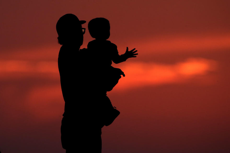 FILE - This photo from Friday June 26, 2020, shows a silhouette against the sky of a man holding a child, as they watch the sunset from a park in Kansas City, Mo. The chaos unleashed in 2020, amid the coronavirus pandemic, has created space for different voices to speak, for different conversations to be had and for different questions to be asked. (AP Photo/Charlie Riedel, File)