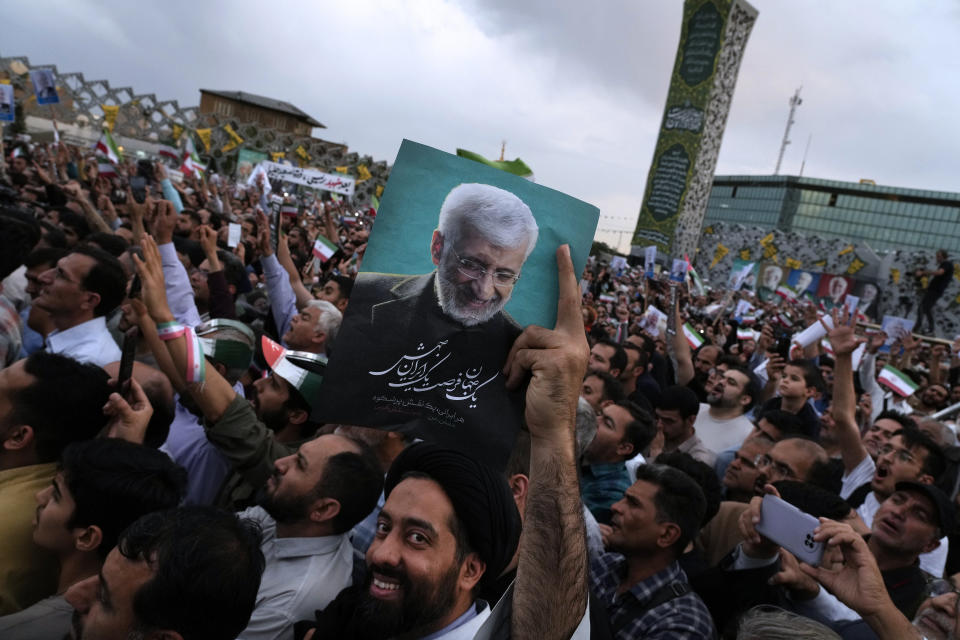 A cleric holds up a poster of Saeed Jalili, a candidate for the June 28, presidential election, during his campaign rally in Tehran, Iran, Monday, June 24, 2024. (AP Photo/Vahid Salemi)