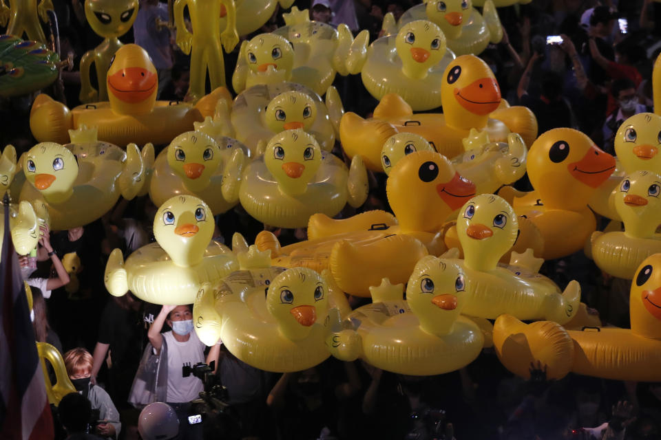 Inflatable yellow ducks, which have become good-humored symbols of resistance during anti-government rallies, are lifted over a crowd of protesters Friday, Nov. 27, 2020 in Bangkok, Thailand. Pro-democracy demonstrators are continuing their protests calling for the government to step down and reforms to the constitution and the monarchy, despite legal charges being filed against them and the possibility of violence from their opponents or a military crackdown. (AP Photo/Sakchai Lalit)