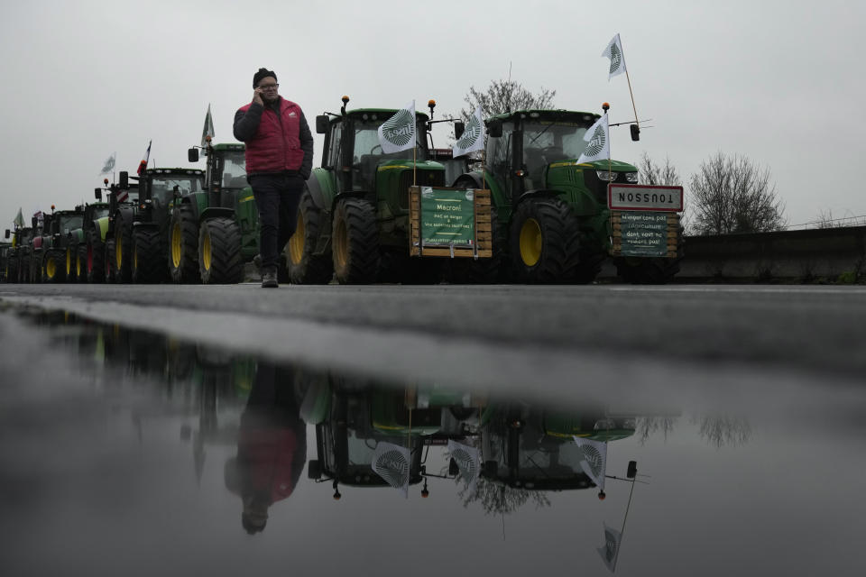 A farmer walks past tractors on a blocked highway, Thursday, Feb.1, 2024 in Chilly-Mazarin, south of Paris. Protests have been held across the EU for most of the week and hundreds of angry farmers driving heavy-duty tractors arrived at European Union headquarters, bent on getting their complaints about excessive costs, rules and bureaucracy heard and fixed by EU leaders at a summit Thursday in Brussels, Belgium. (AP Photo/Christophe Ena)