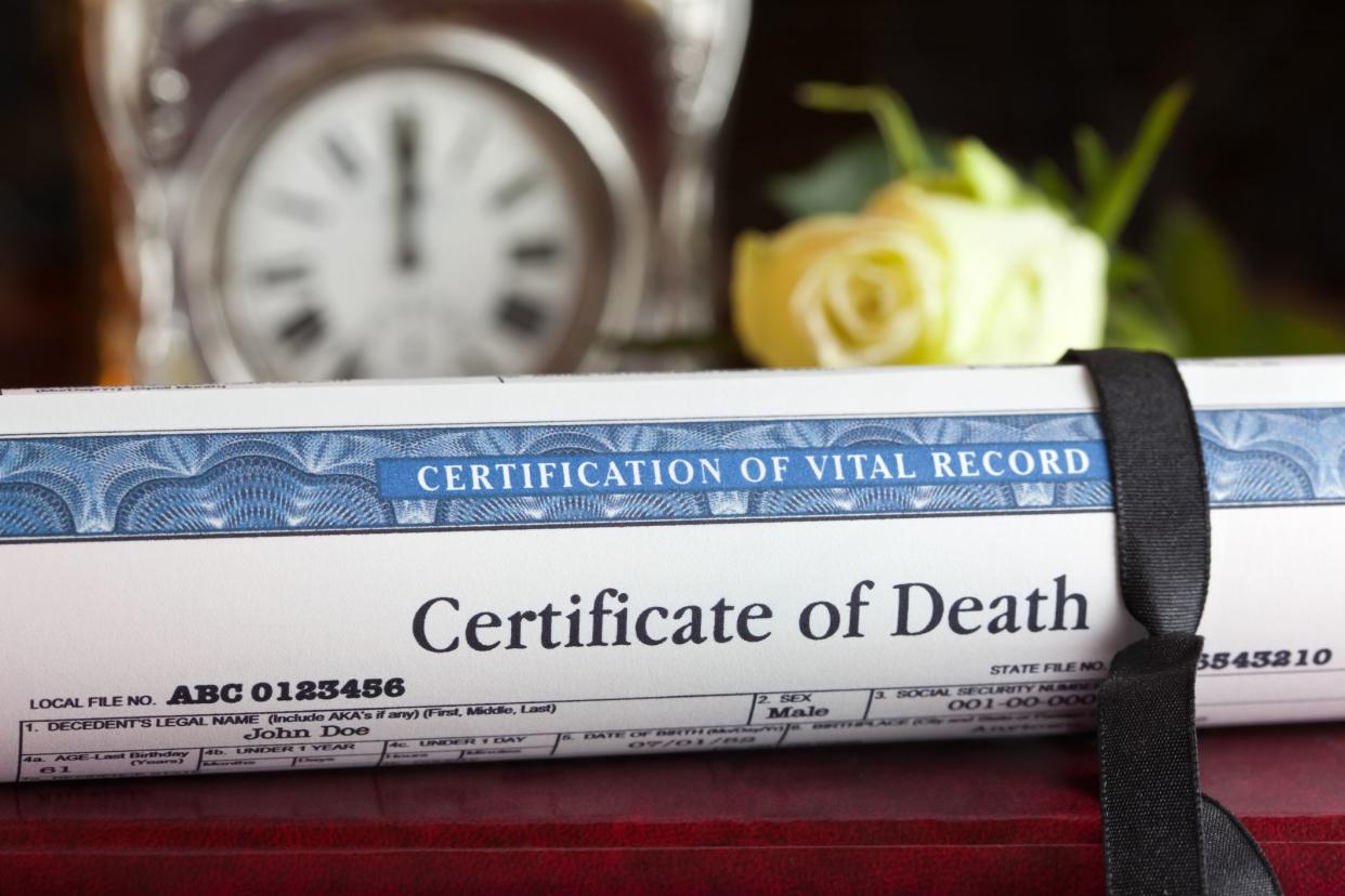 rolled up death certificate with flowers in the background