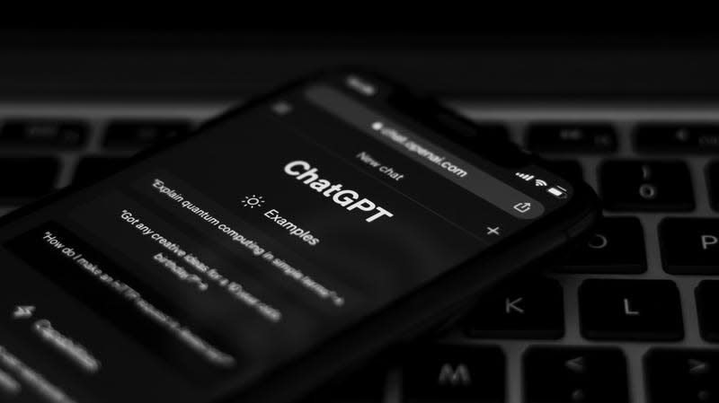 Webpage of ChatGPT, a chatbot prototype on the OpenAI website on a smartphone. In the background is a computer keyboard.